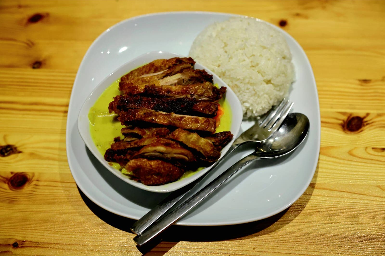 Knuspriges Hähnchen auf Curry-Sauce, daneben Reis, auf einem weißen Teller